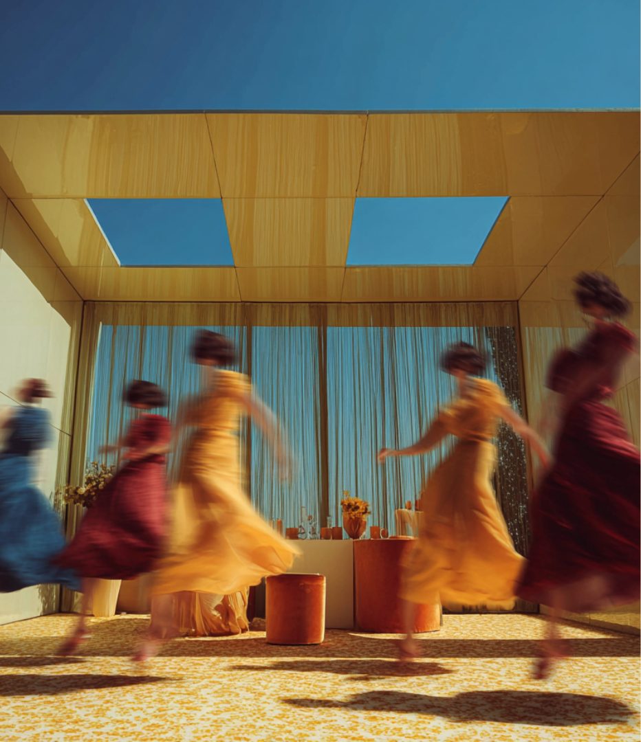 Performers in flowing dresses moving through a golden, sunlit set